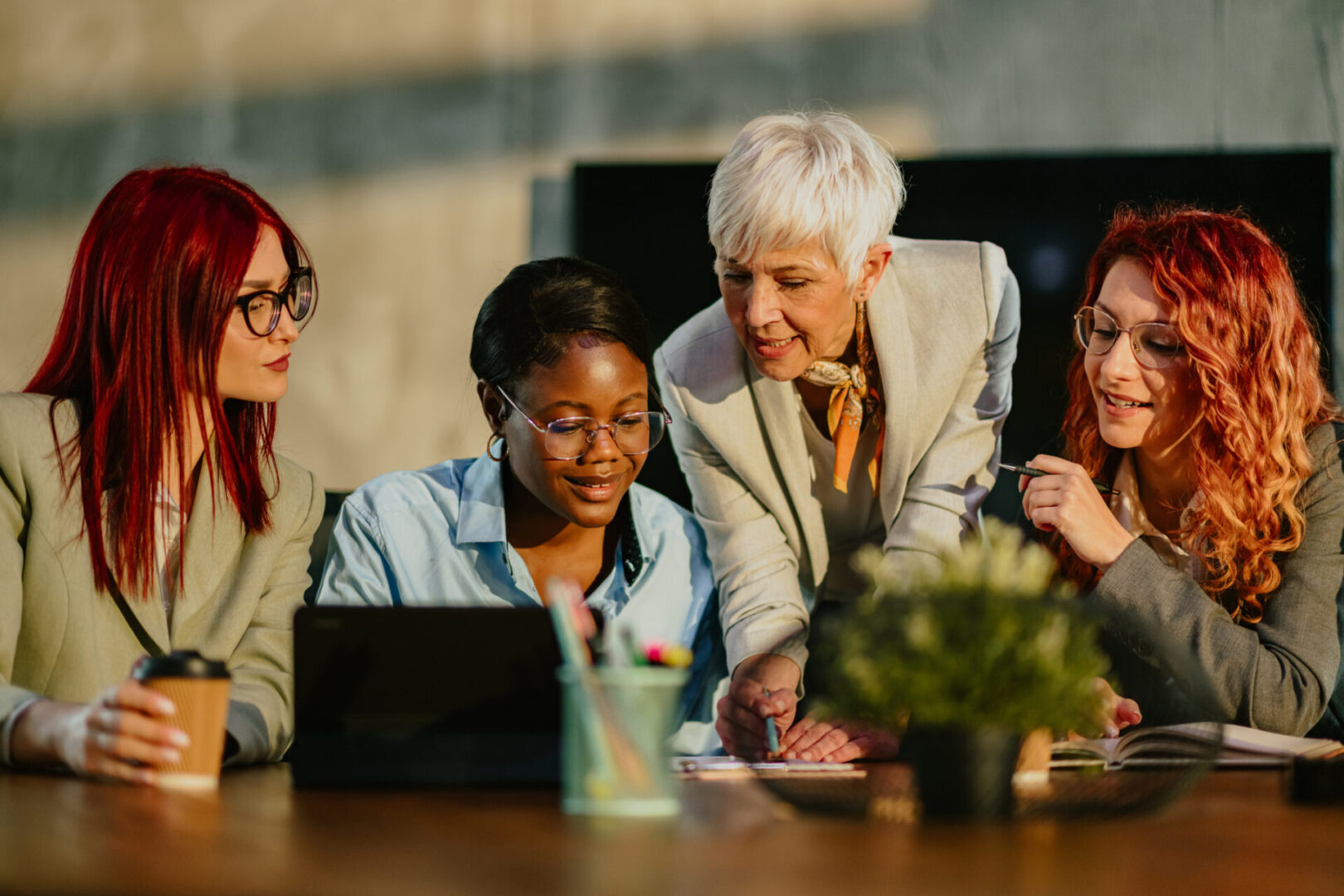 Senior businesswoman is standing at boardroom with her multicultural team and tutoring them. Mature female mentor is teaching her interracial team new business strategies and analyzing data with them.